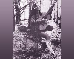 Buffy Sainte Marie holding her guitar in the forest